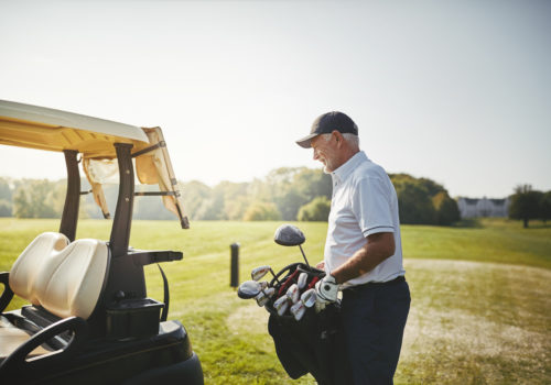 Senior man putting his bag full of clubs on a cart while enjoying a round of golf on a sunny day